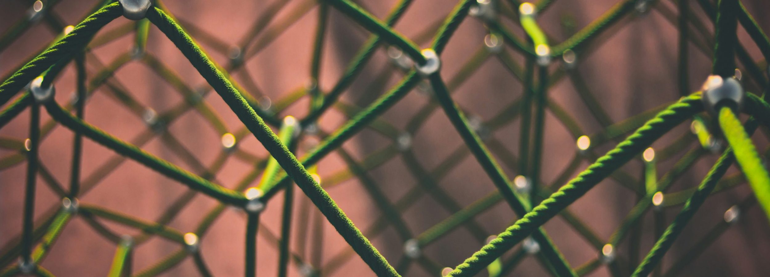 A close up of a 3D network of green ropes, connected by nodes of small silver spheres.